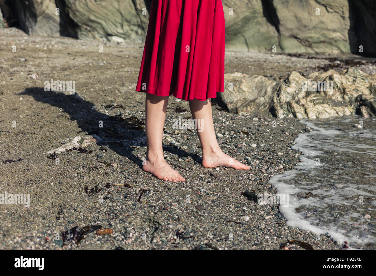 The feet of a young woman in a red dress as she is walking on a beach ...