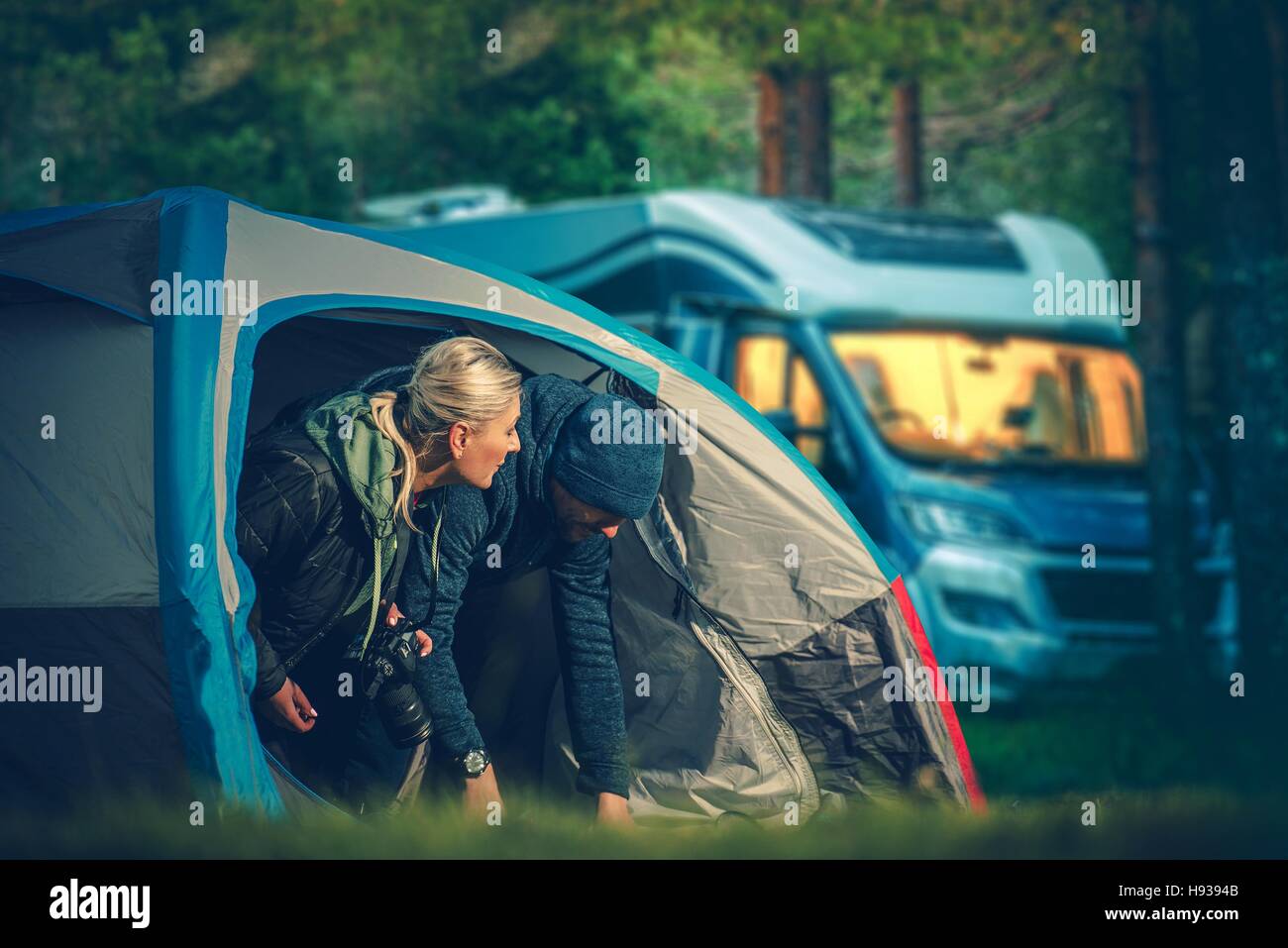 Couples Tent Camping. Men and Woman in Their 30s Camping in the Small Tent with Motorhome in the Background. Stock Photo
