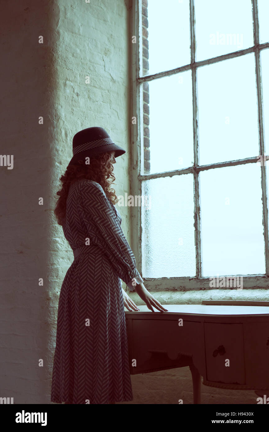 Woman In Vintage Dress And A Hat Leaning On Dresser And Looking