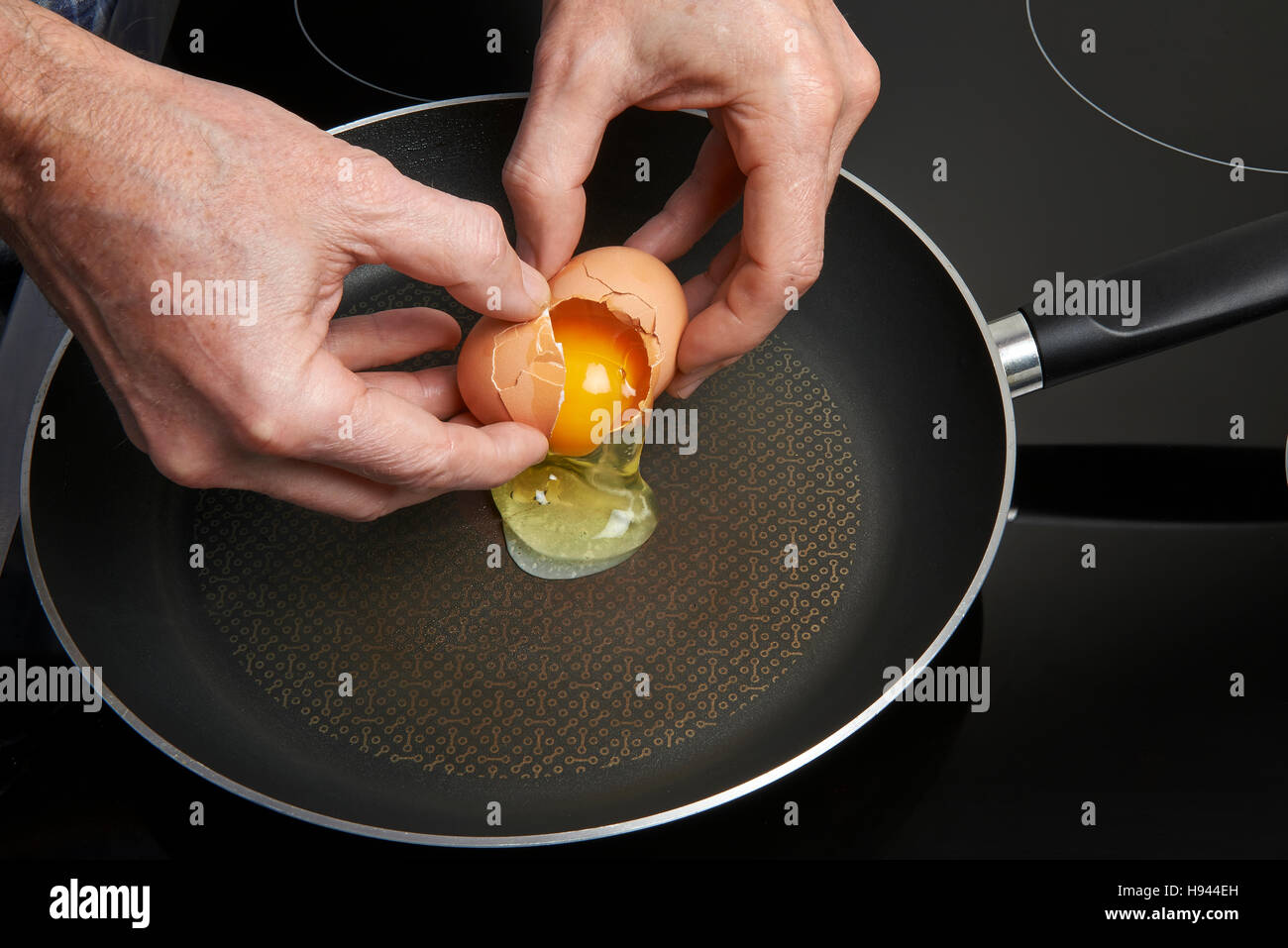 Man's hand above frying pan with cooked eggs Stock Photo