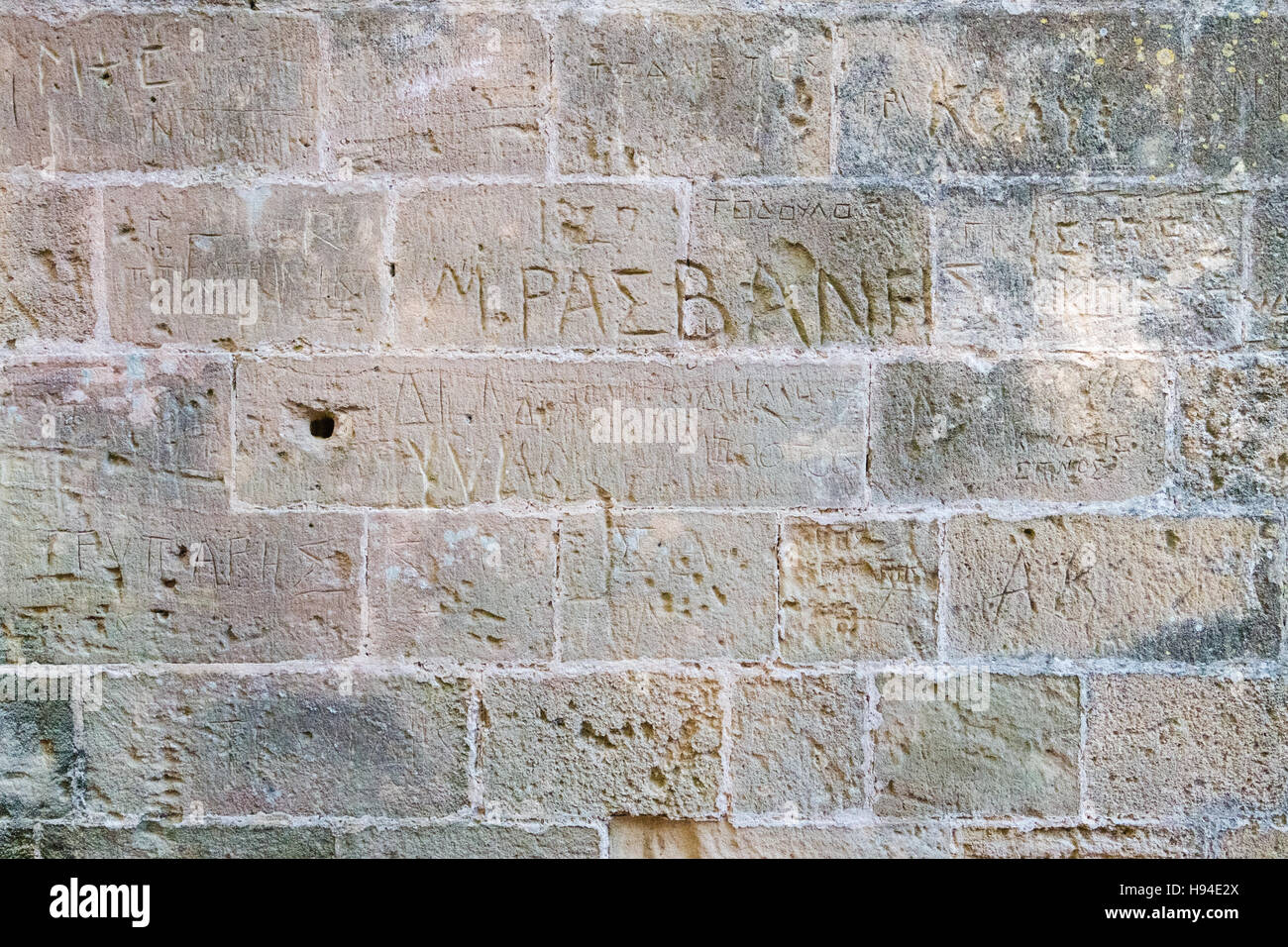 Old brick wall background with Greek graffiti carved into it. Stock Photo