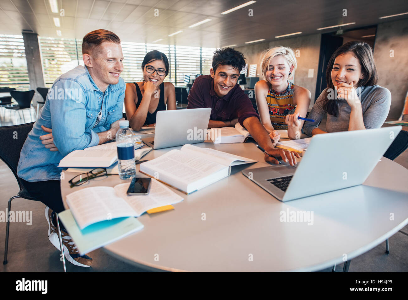 Multiethnic group of young people studying together at a table looking at laptop. Young students in cooperation with their school assignment. Stock Photo