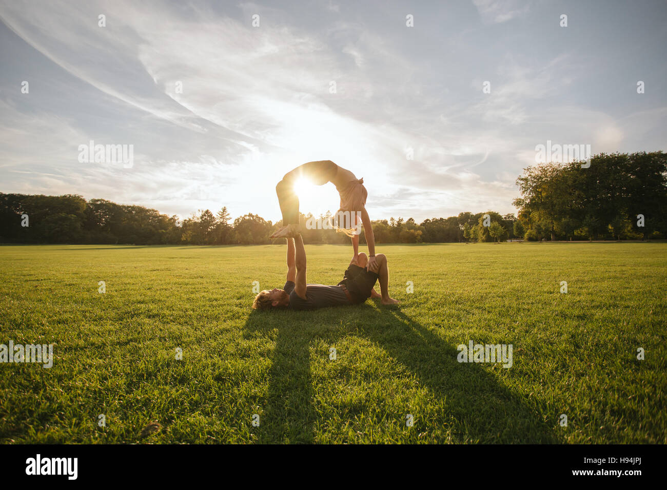 Shot of young couple doing acrobatic yoga on lawn. Young man lifting and balancing woman at the park. Stock Photo