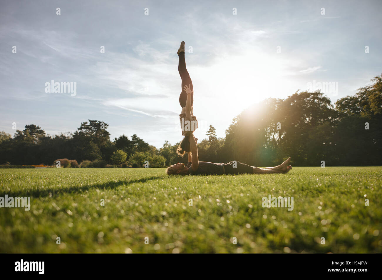 Healthy young couple doing pair yoga outdoor in park. Man lifting and balancing woman in park. Stock Photo
