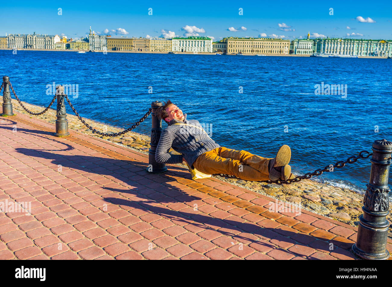 SAINT PETERSBURG - APRIL 24, 2015: Young man in good mood lying on chains on the embankment of Neva River, on April 24 in Saint Petersburg. Stock Photo