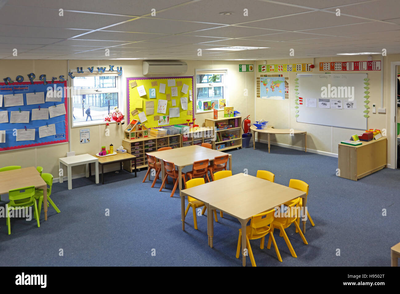 Brightly coloured interior of a modern year 1 school classroom showing tables, chairs shelves and artwork on walls Stock Photo