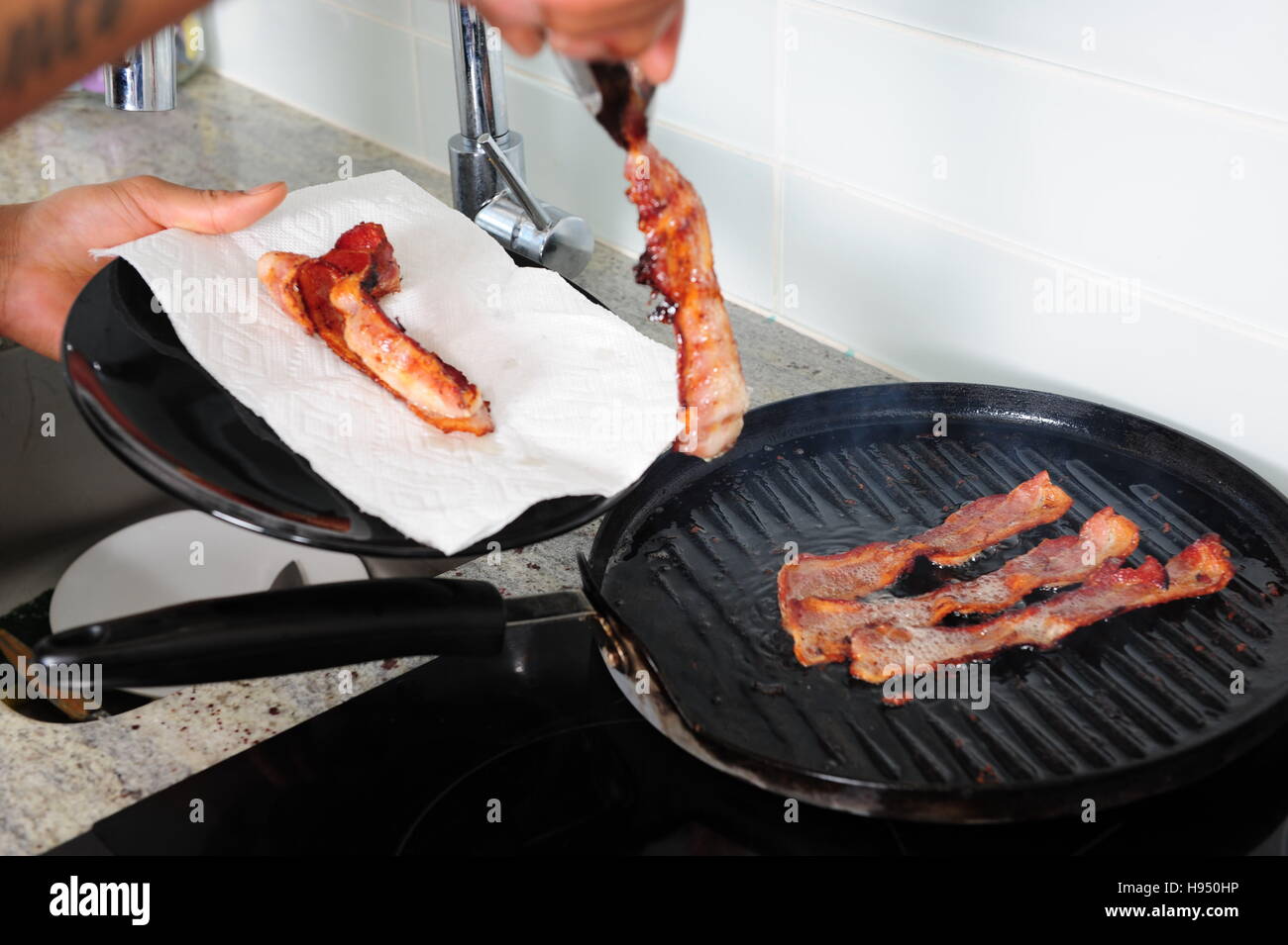 African American man cooking bacon on stove with a grill pan Stock Photo
