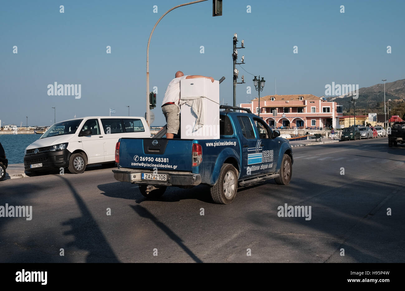 A man on the back of a van holding a fridge in Zakynthos Stock Photo