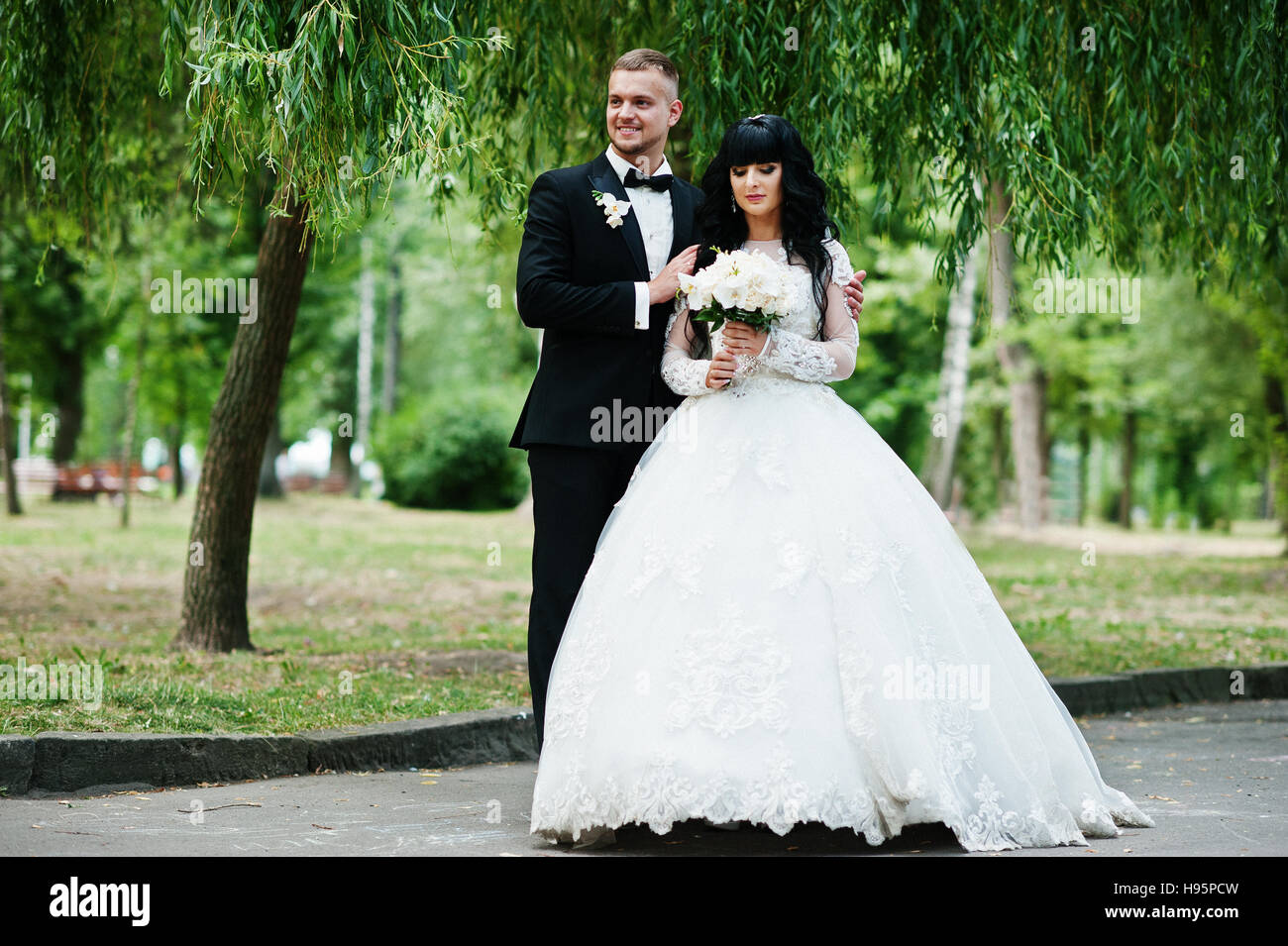 Delectable wedding couple stay hugging on park background willow tree. Stock Photo