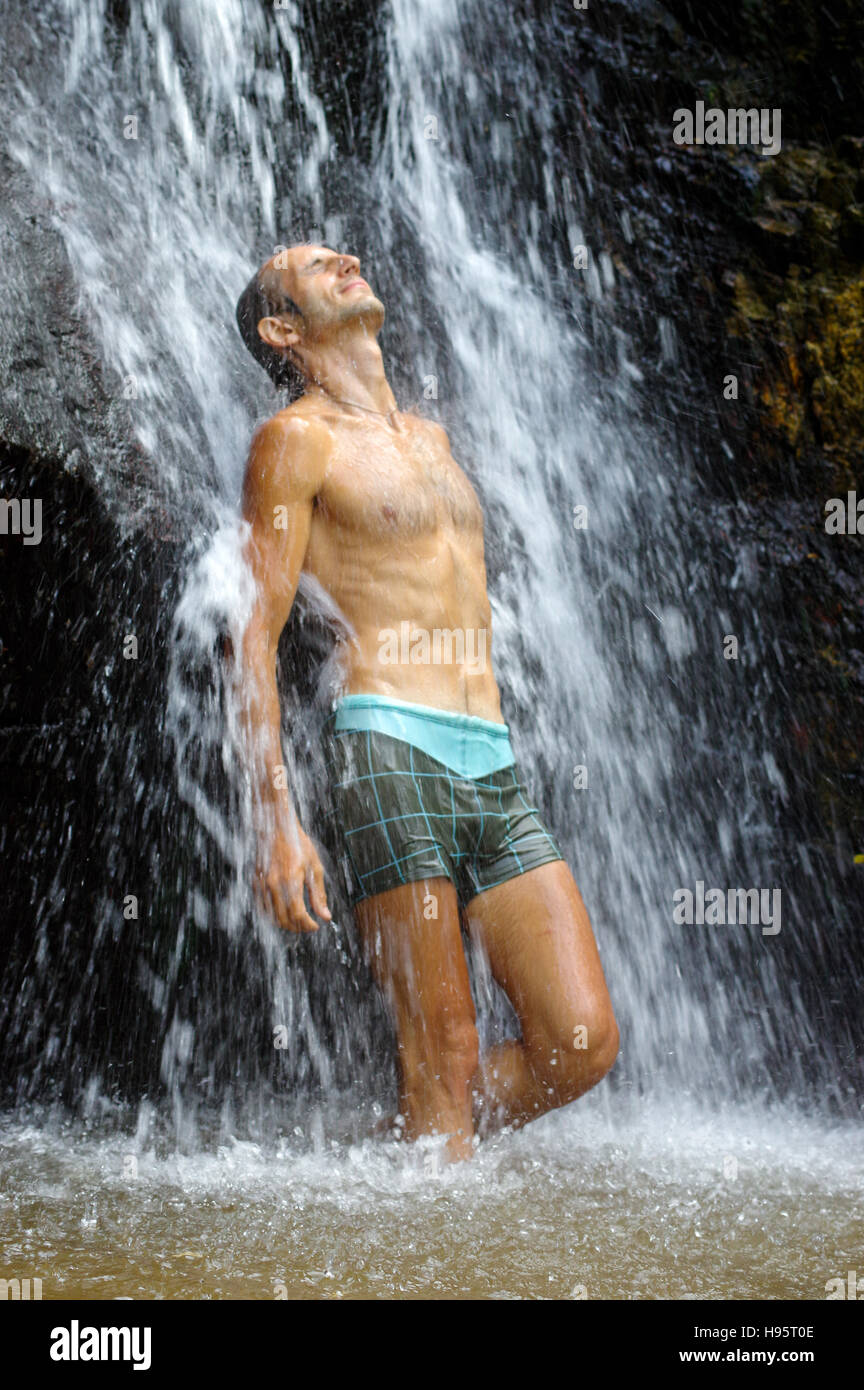 a man taking a relaxing shower under a waterfall outside Stock Photo