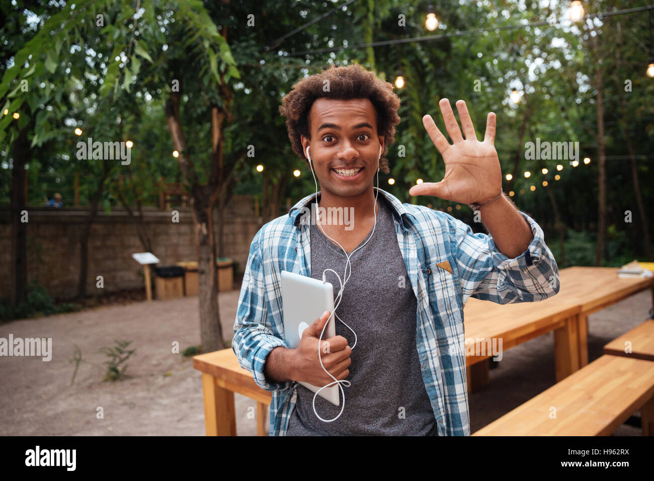 Cheerful african young man with tablet standing outdoors and saying hello Stock Photo