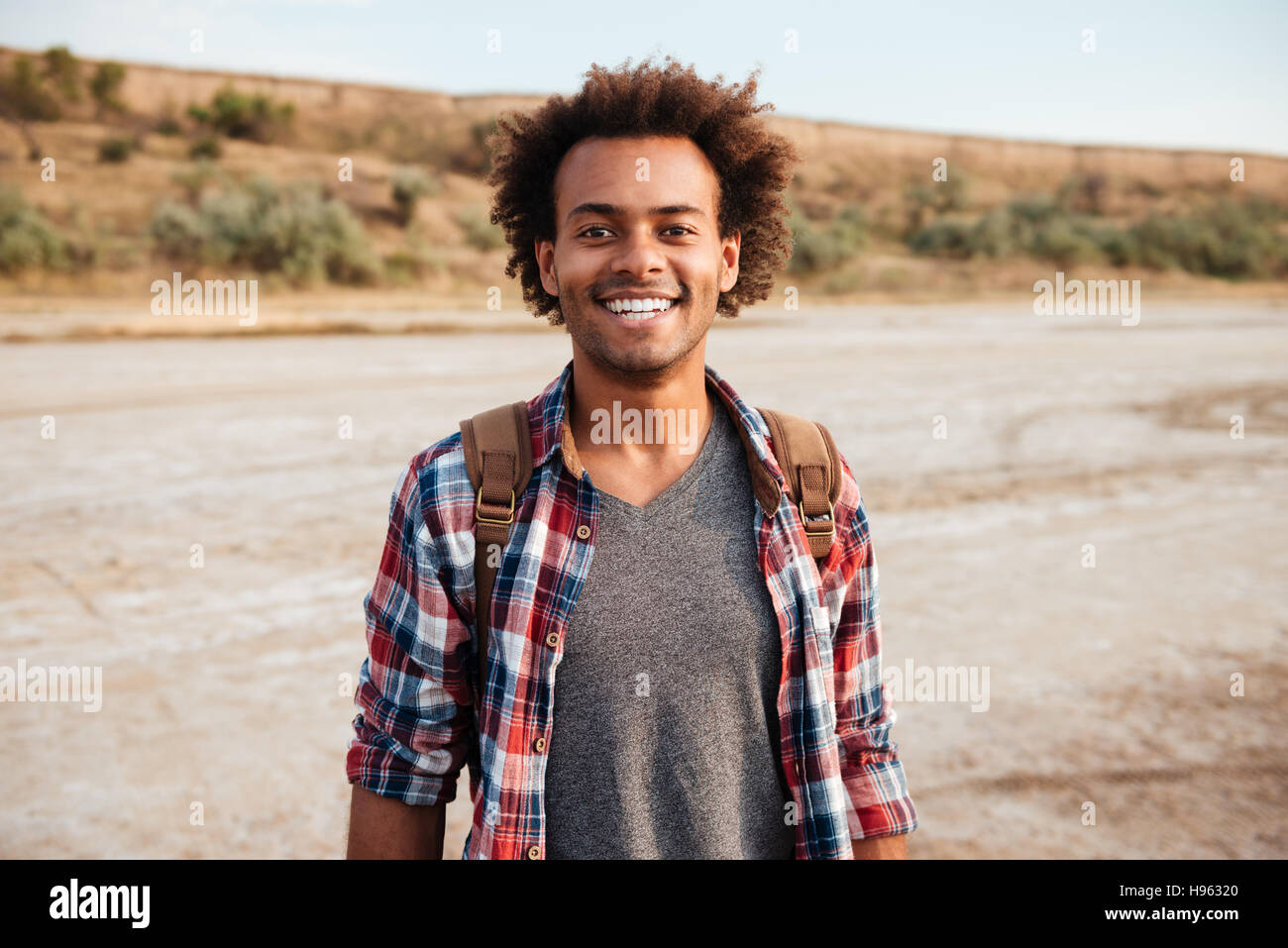Portrait of cheerful african american young man in plaid shirt with backpack Stock Photo