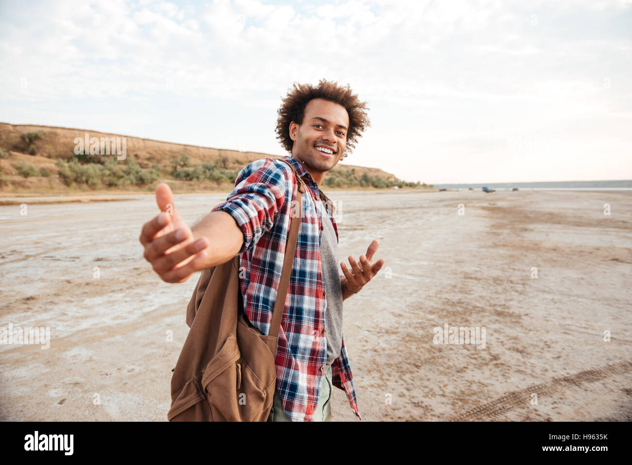 Happy african american young man with backpack inviting you to go with him Stock Photo