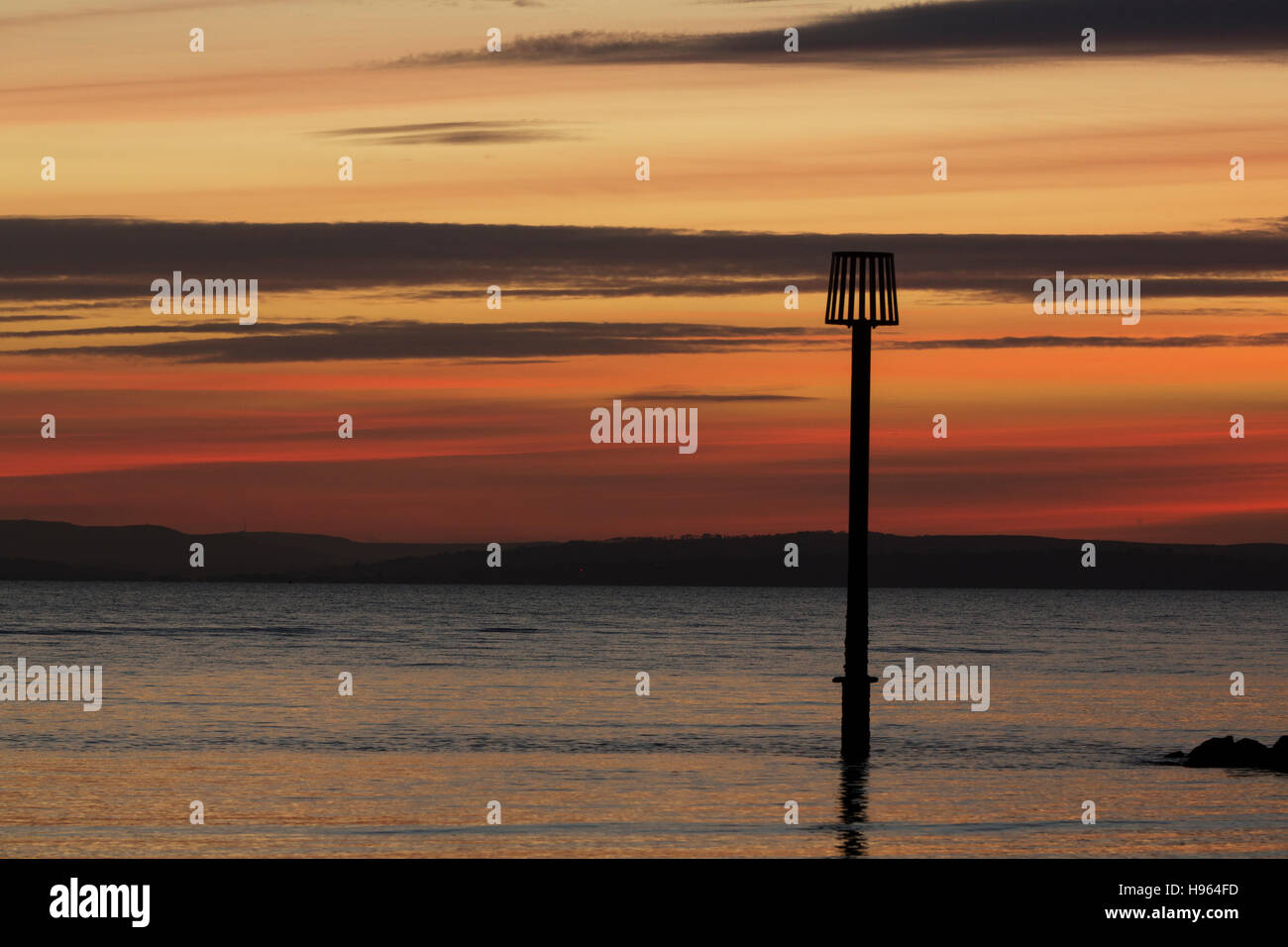 Beach marker sign in the sea against a vivid sunset. Calm sea and land beyond. Colorful sky off Hayling Island Hampshire Stock Photo