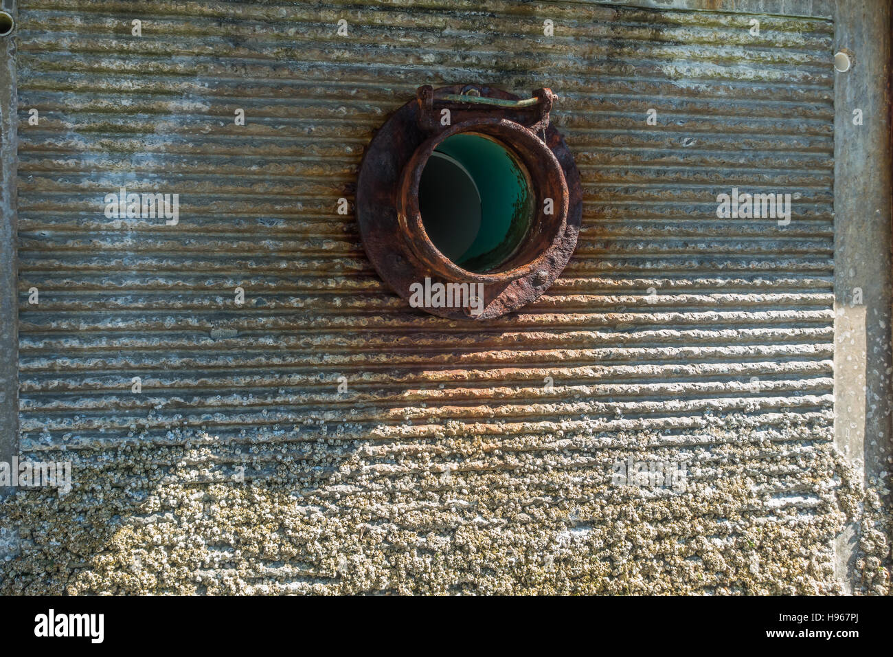 A rusted fitting encircles a sewer pipe exiting a wall. Stock Photo