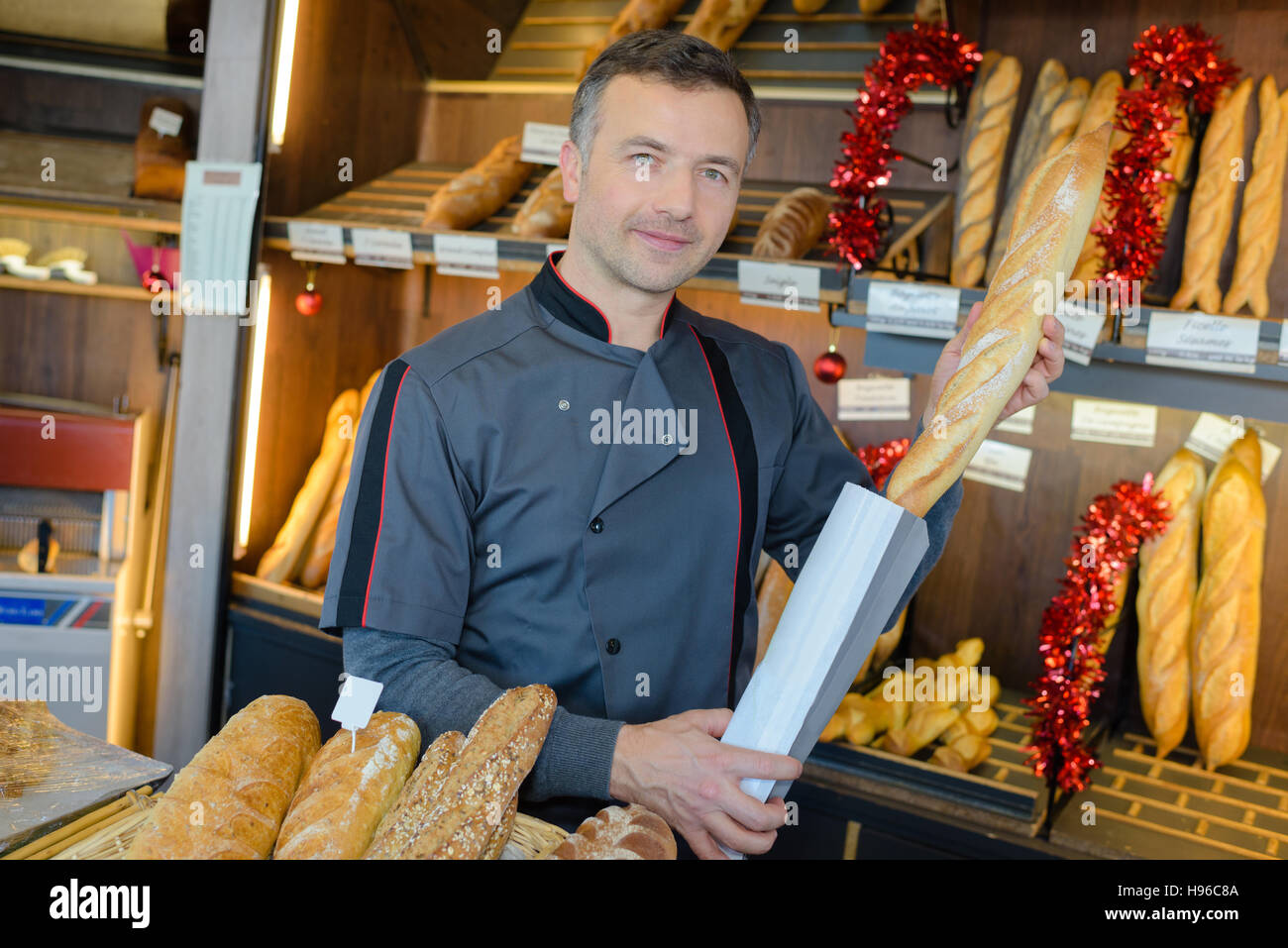 Baker putting baguette in paper bag Stock Photo - Alamy