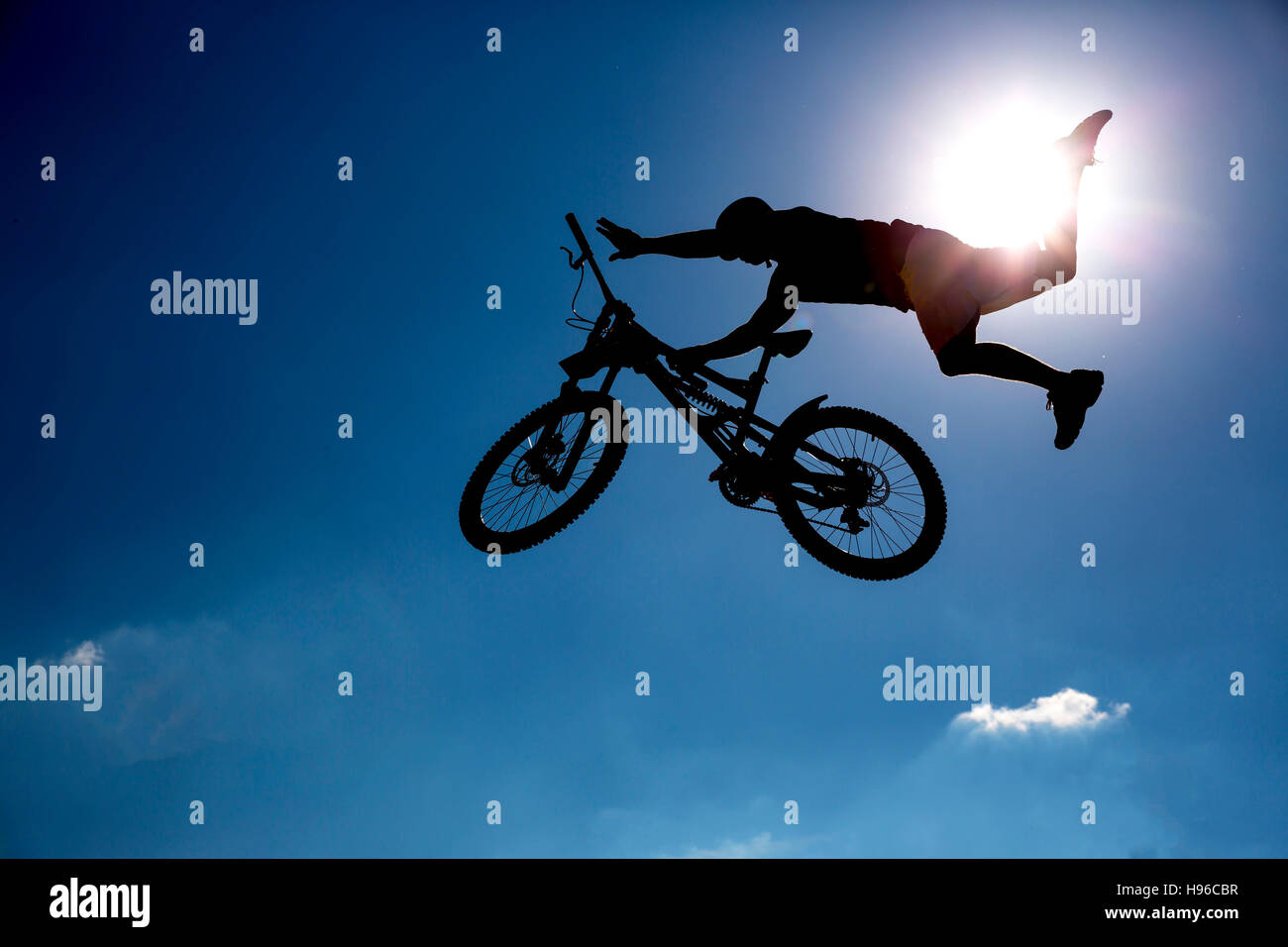 Silhouette of a biker jumping against the blue sky and the sun. Stock Photo