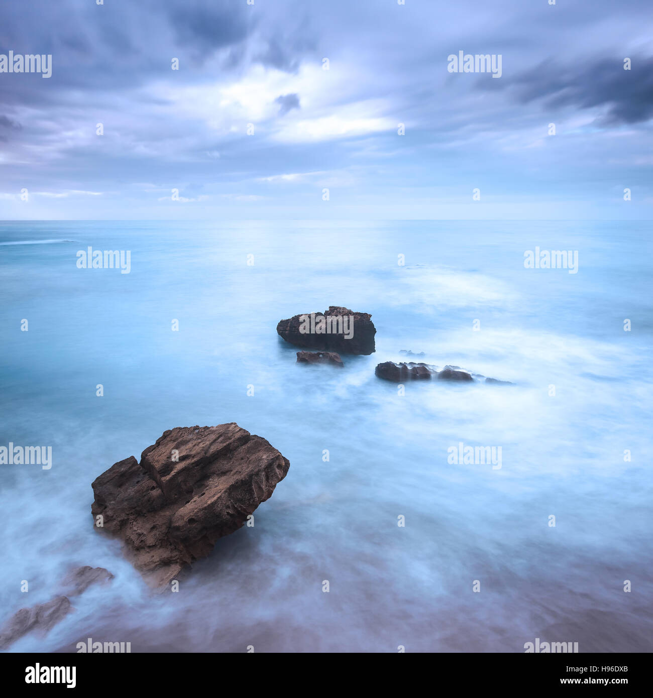 Rocks in a blue ocean waves under cloudy sky in a bad weather. Long exposure photography Stock Photo