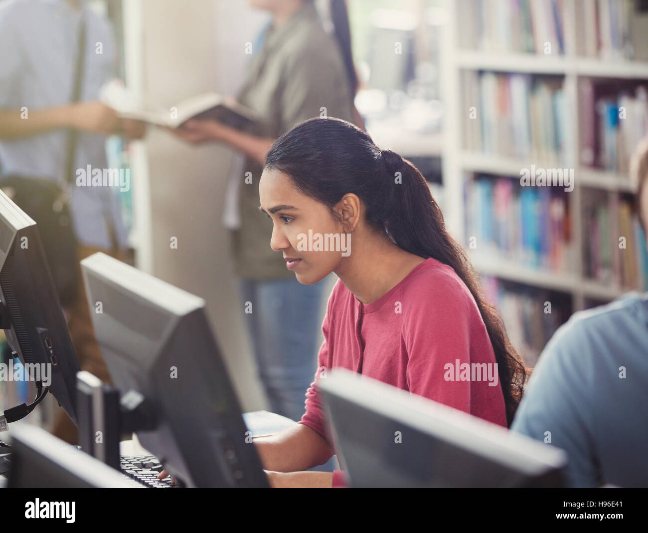 Focused female college student researching using computer in library ...