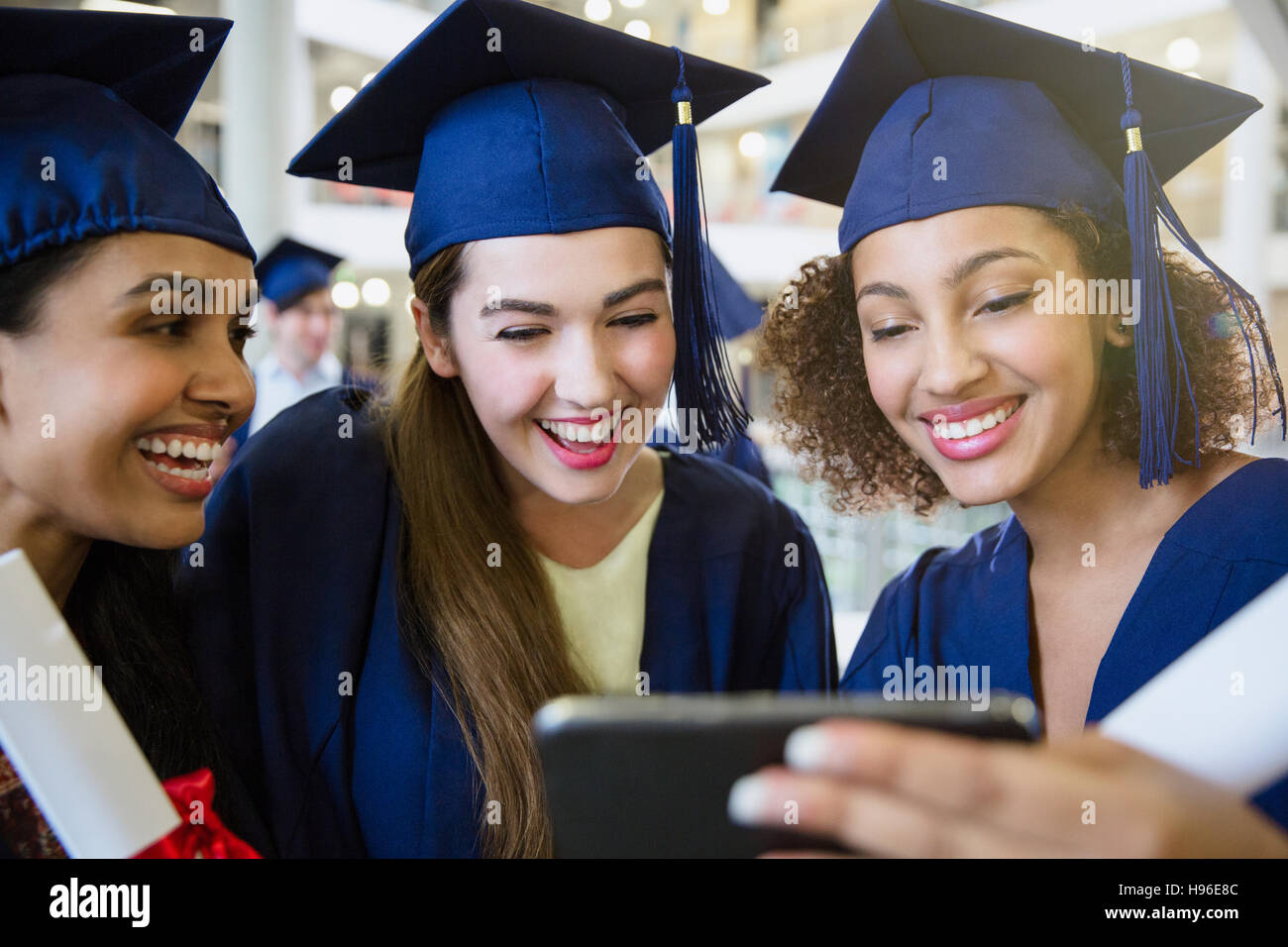 Smiling college graduates in cap and gown using cell phone Stock Photo