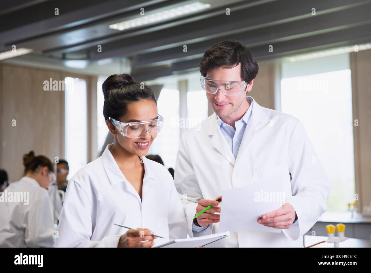 College students in lab coats discussing notes in science laboratory classroom Stock Photo