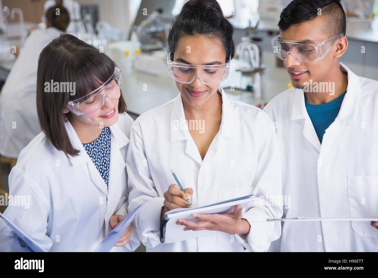 College students in lab coats discussing notes in science laboratory
