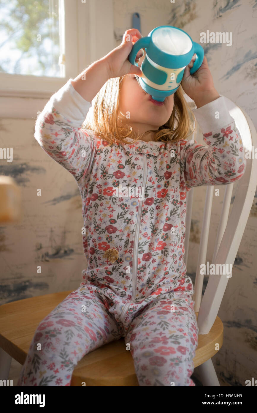 Girl (23) sitting on chair and drinking milk from sippy cup Stock