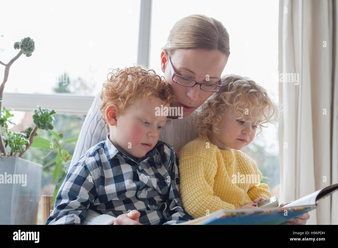 Mother reading to children (4-5, 8-9) in living room Stock Photo