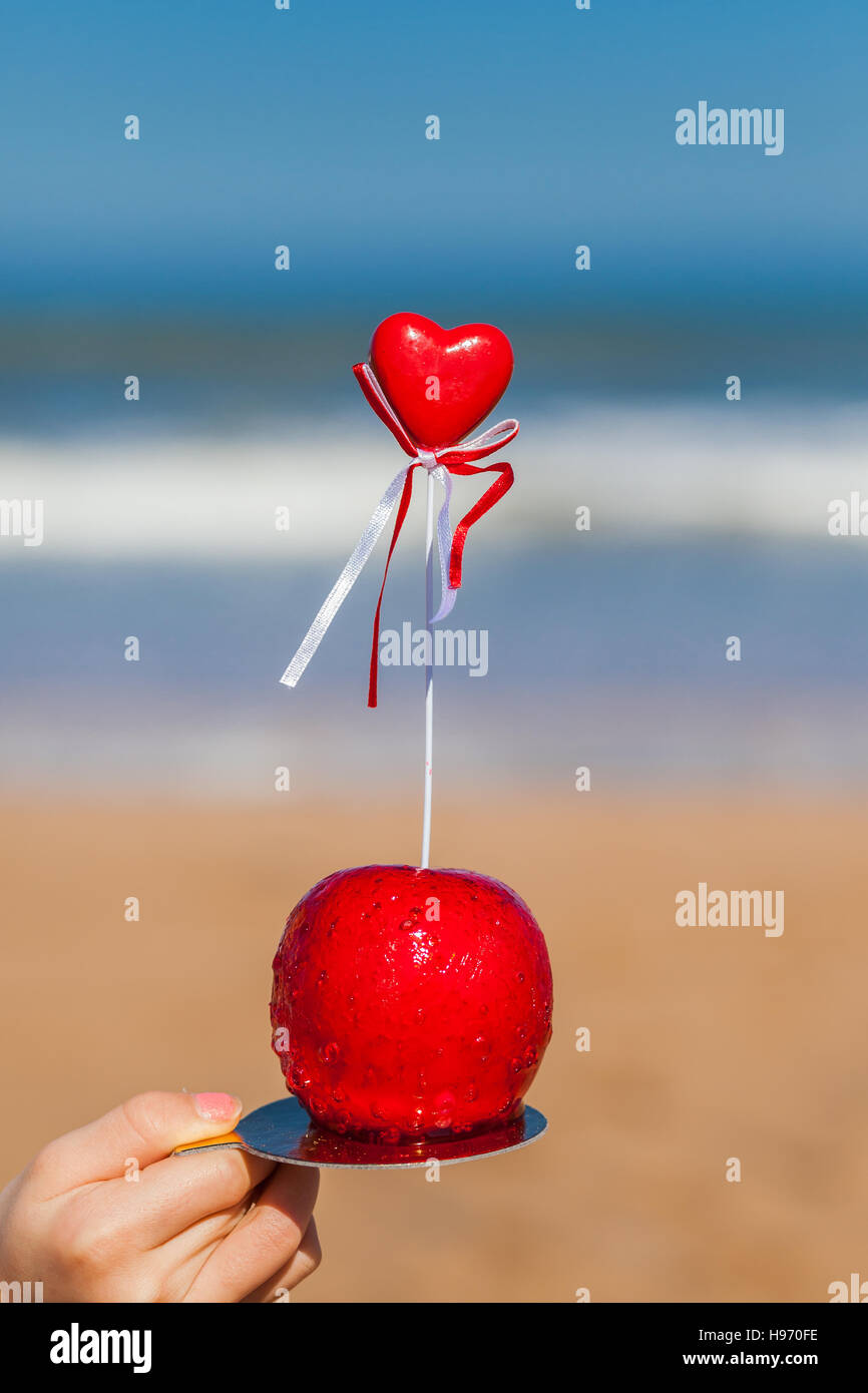 Female hand hold a red candy apple with red heart on top Stock Photo