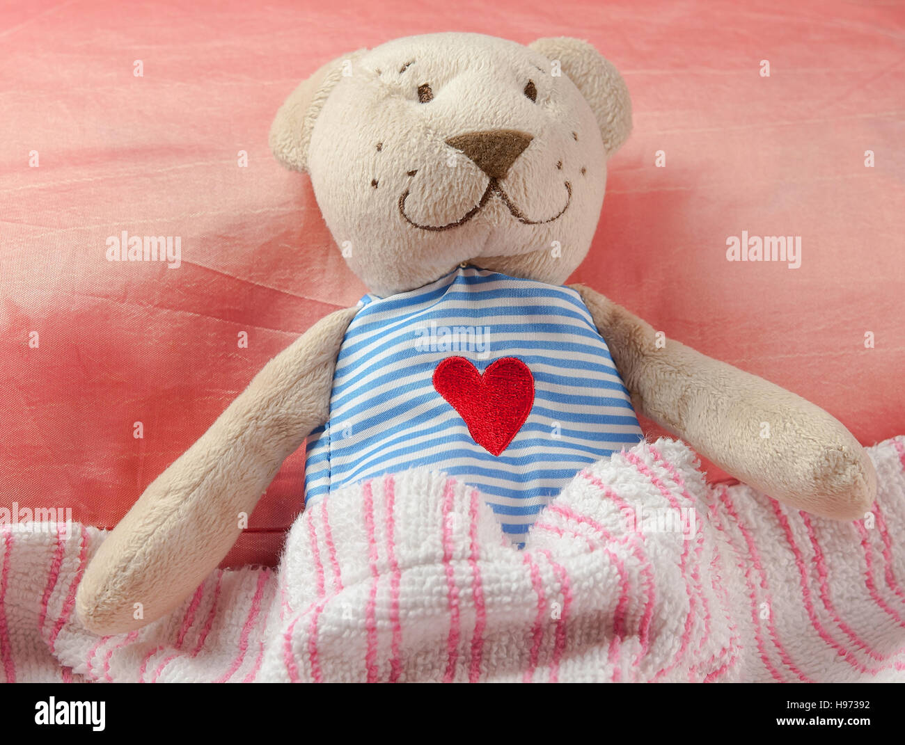 adorable teddy bear laying in bed, under the sheets. Stock Photo