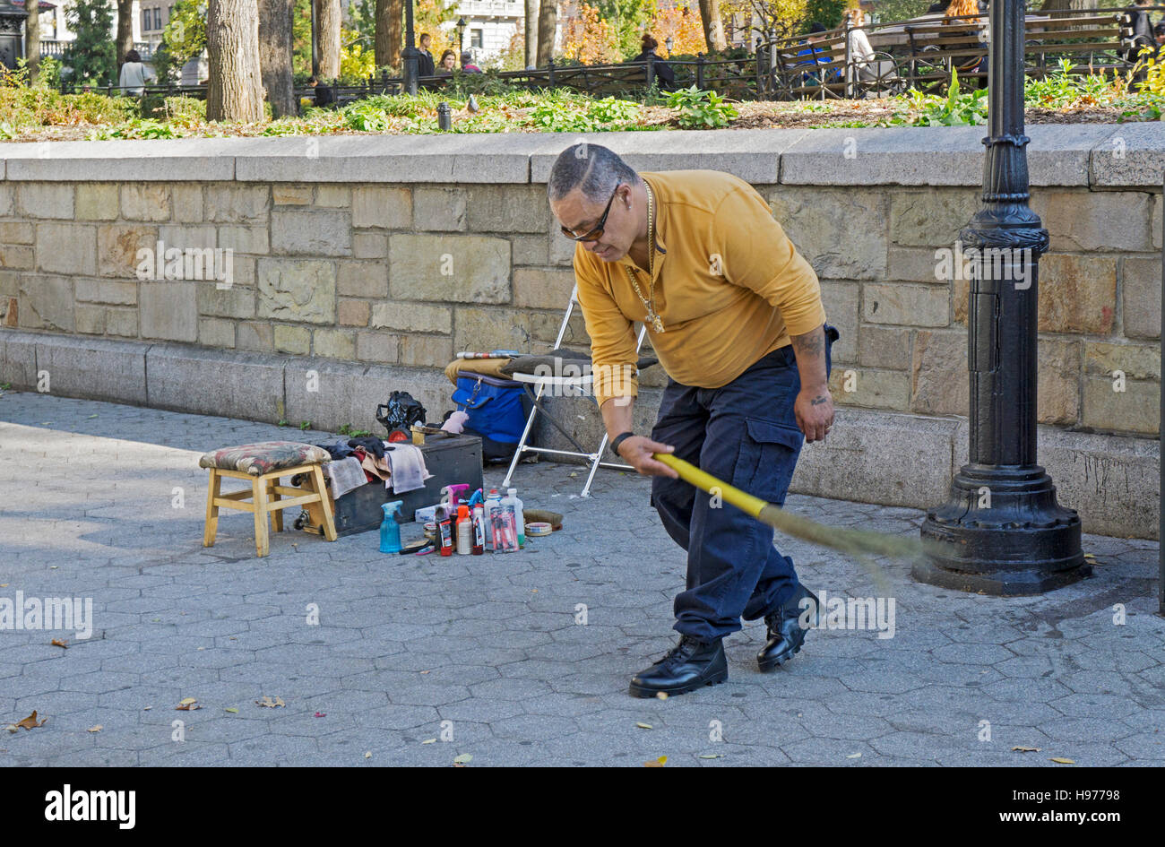 A shoeshine man cleans the area around his stand with an old fashioned straw broom. In Union Square Park in New York City. Stock Photo