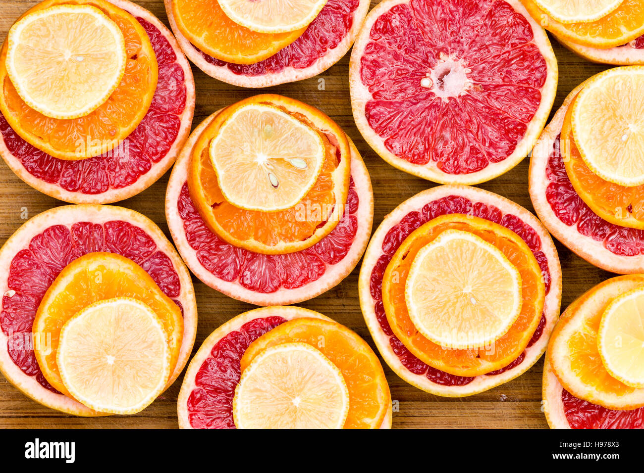 Full Frame, High Angle View of Sliced Ruby Red Grapefruit Stacked with Ripe Orange and Lemon Slices on Rustic Wooden Cutting Board Stock Photo