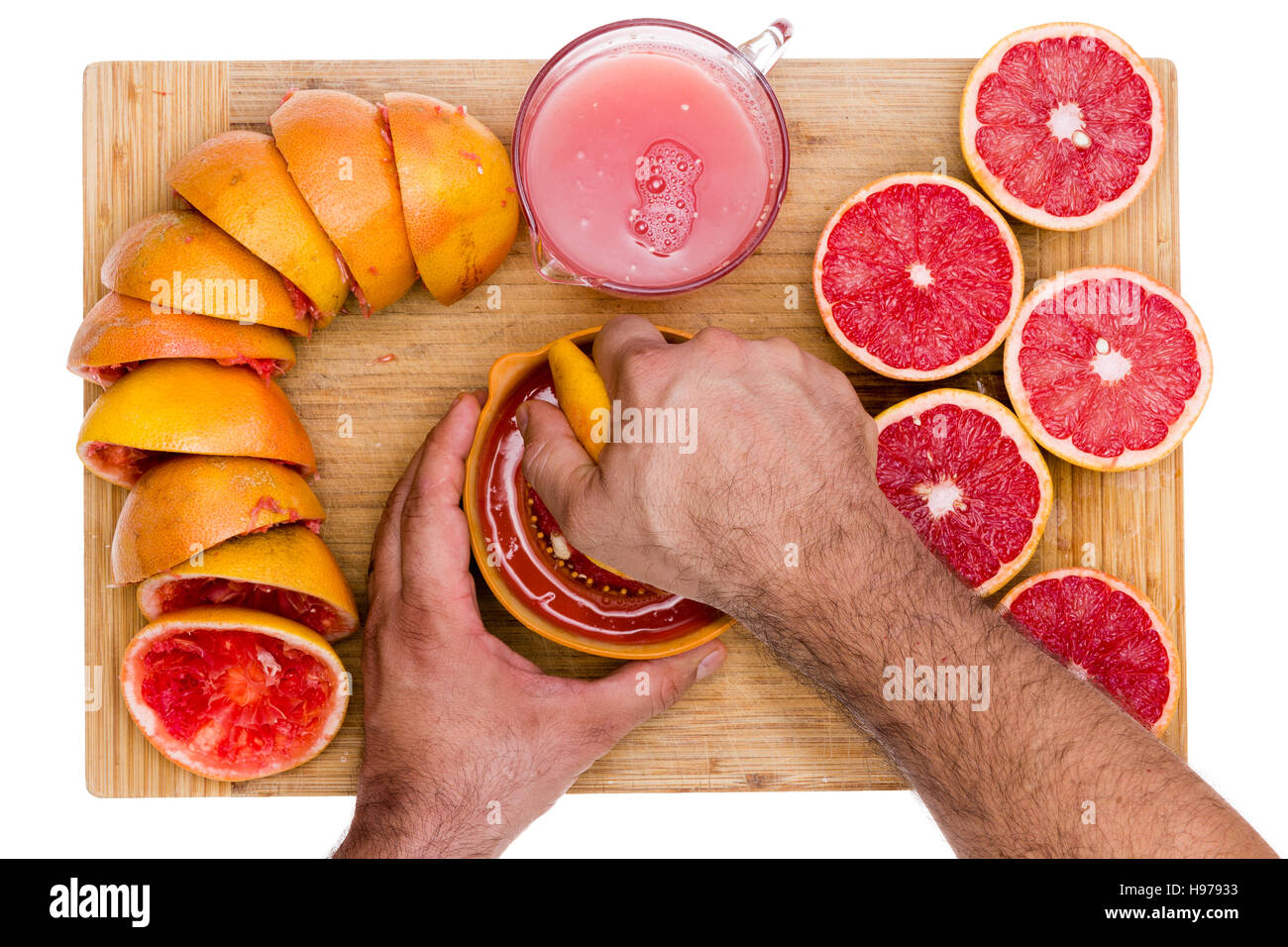Hands of a man squeezing fresh ruby grapefruit halves on a manual juicer with fresh cut juicy fruit on one side and squeezed skins on the other on a b Stock Photo