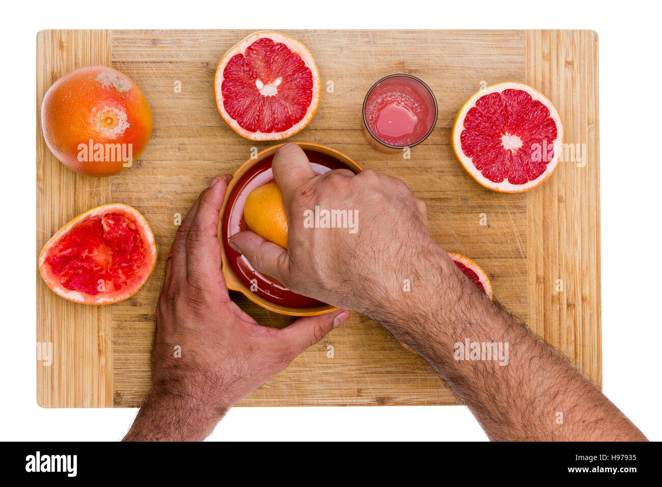Man squeezing cut fresh ruby grapefruit halves on a manual juicer with a glass of fresh juice rich in pectin soluble fiber alongside, overhead view of Stock Photo