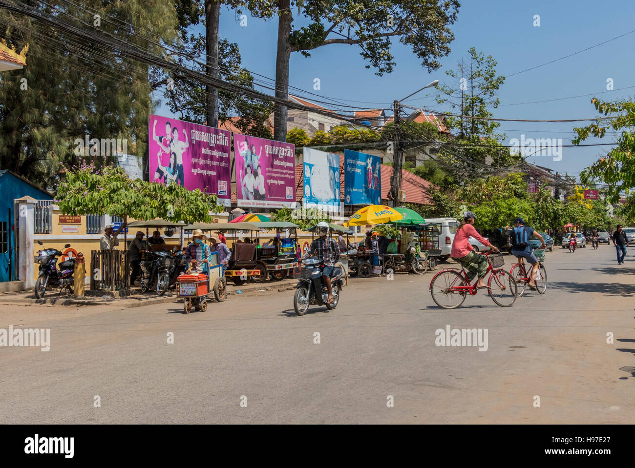 Cyclist and motorcyclist on road with vendors selling food and drink in Siem Reap Cambodia Stock Photo