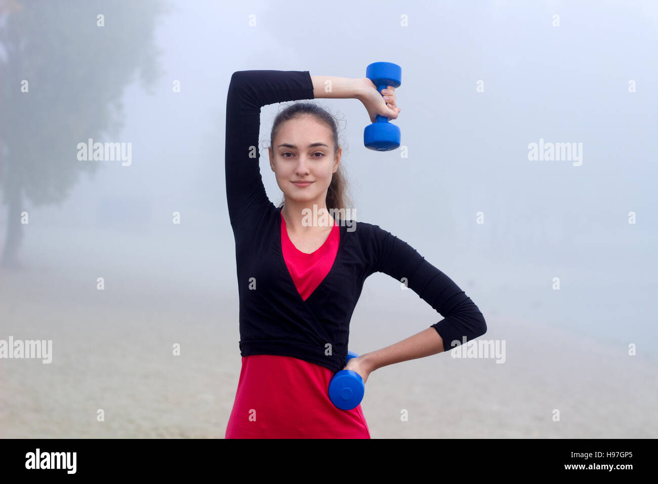 Young pretty slim fitness sporty woman exercises with weights dumbells during training workout outdoor Stock Photo