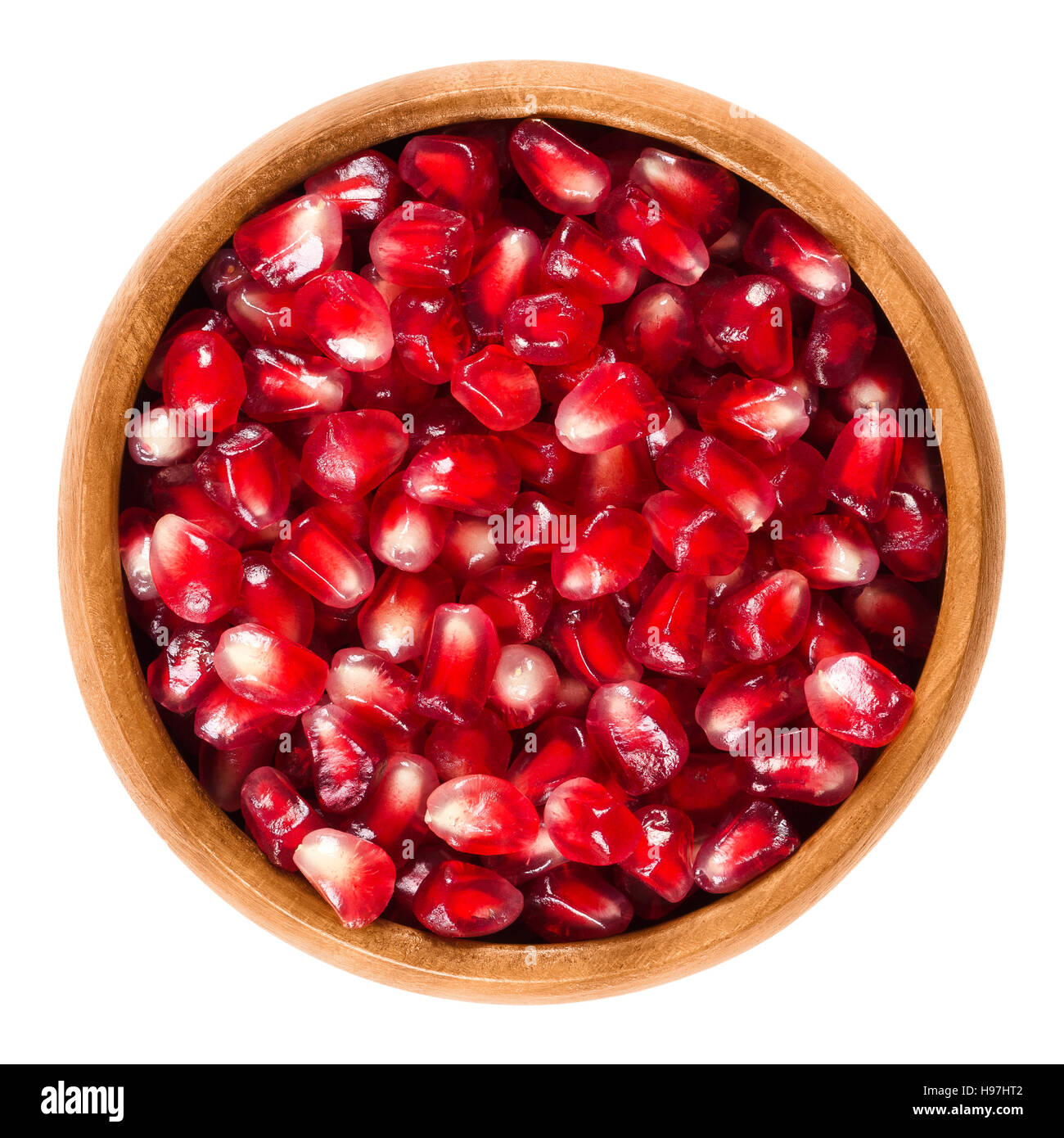 Fresh pomegranate seeds in wooden bowl. Edible red seeds from the fruit of Punica granatum, separated from the peel. Stock Photo