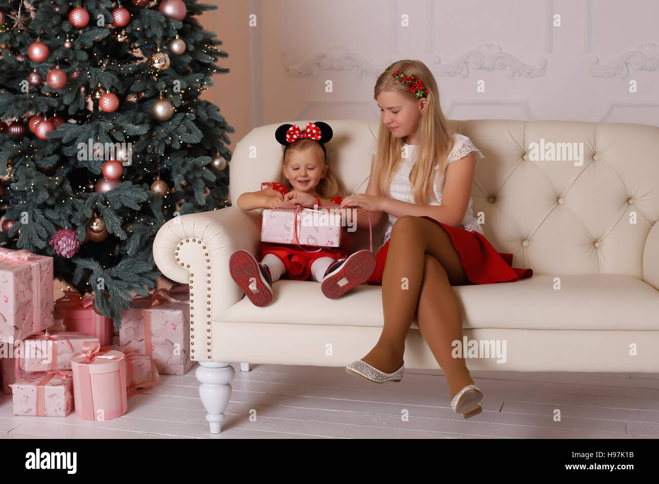 sisters girls sitting on the couch with Christmas gifts in hands Stock Photo