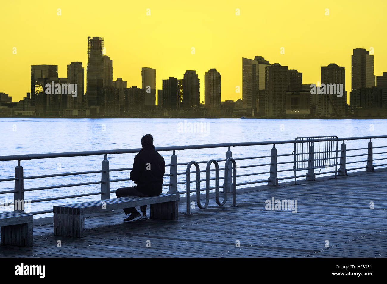 Dual-tone image of a man sitting on park bench watching the sunset over Hudson River in New York City Stock Photo