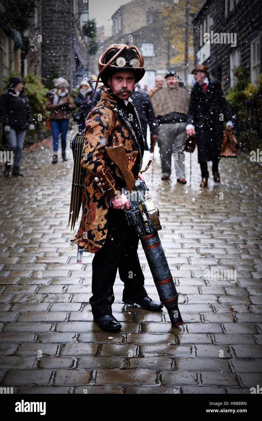 A man, with a mustache, poses dressed in steampunk clothing, with a gun, on a cobbled street in the snow. Stock Photo