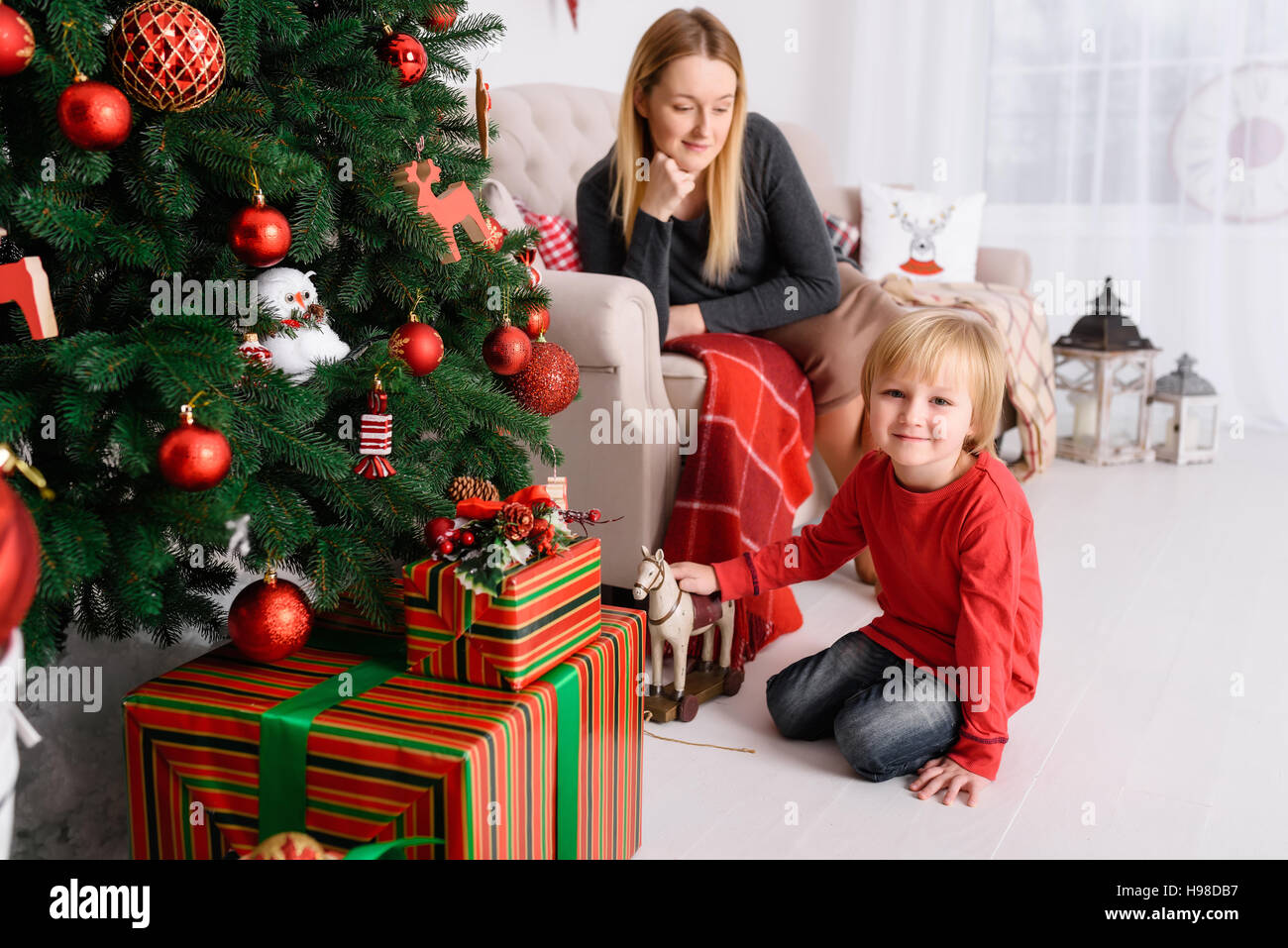 Mom plays with her son near Christmas tree Stock Photo