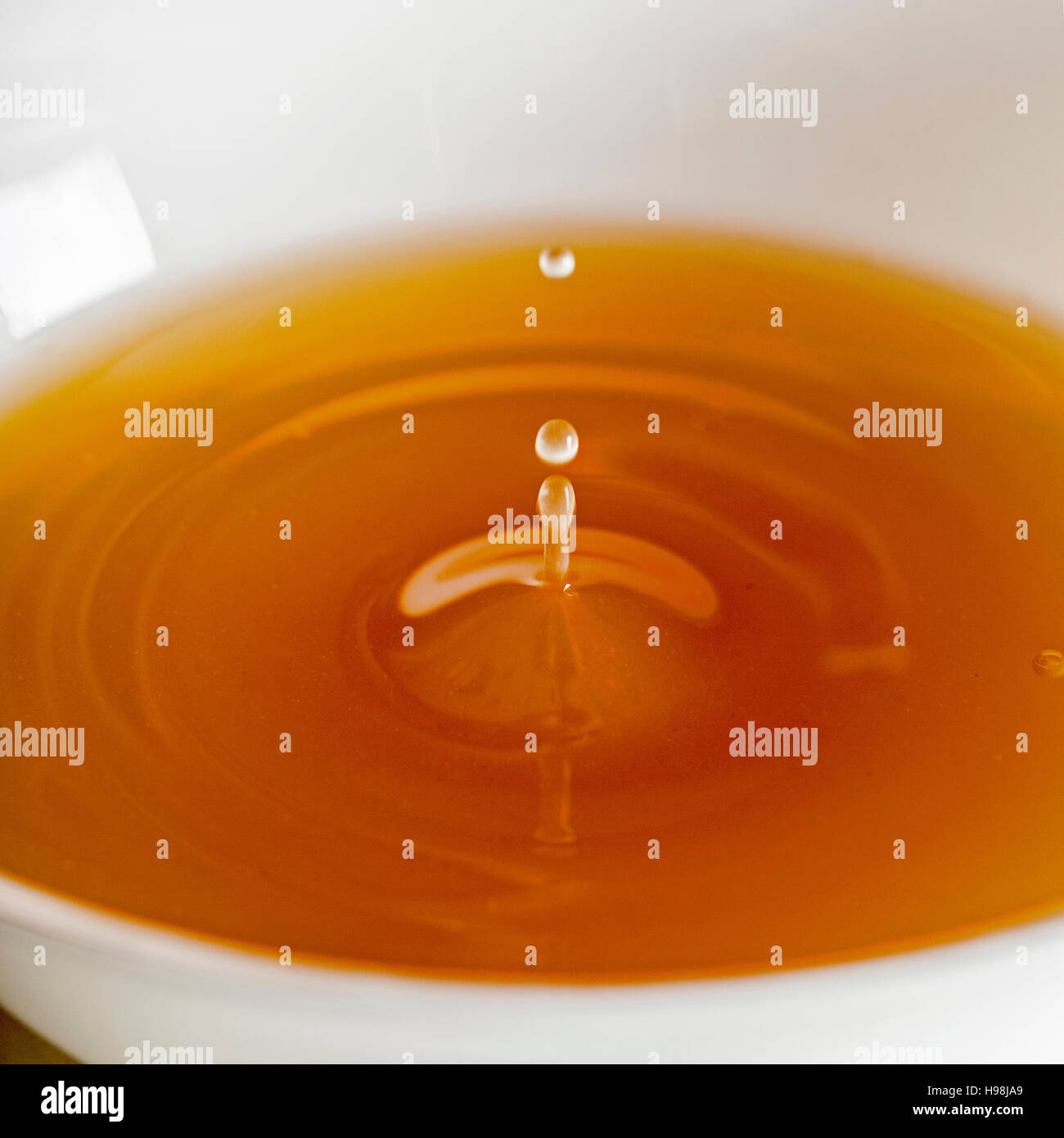 Water drop falling into a broth, clear soup in a white cup Stock Photo