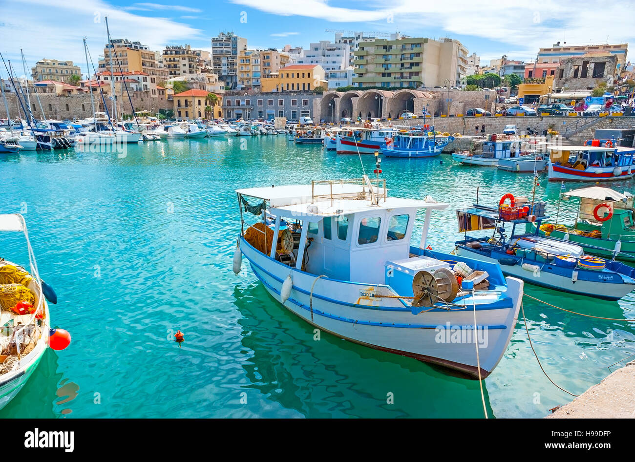 The lazy fishing boats slowly ride on the waves in old harbor,  Heraklion. Stock Photo