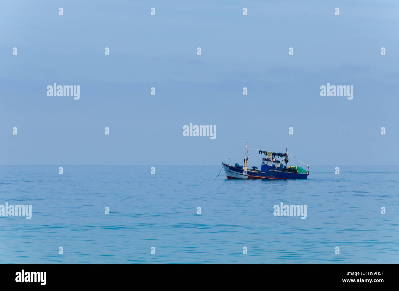 Blue painted small fishing boat in front of the Angolan coast of the Namib Desert. Dominating blue colors and calm mood. Stock Photo