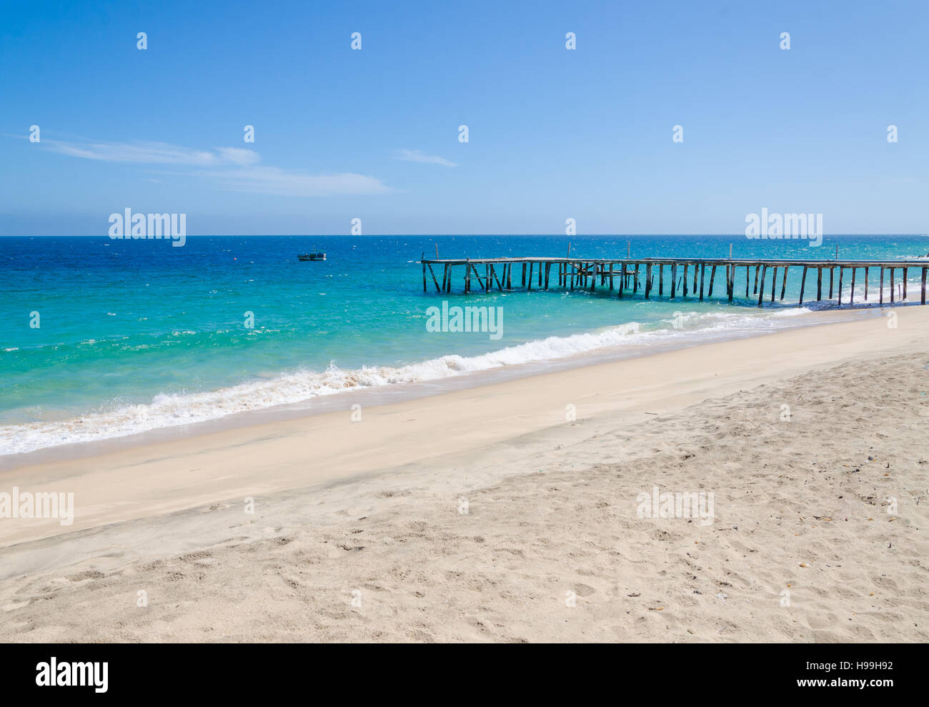 Long simple wooden jetty leading into turquoise blue ocean at small fishing village Mucuio in Angola. Stock Photo