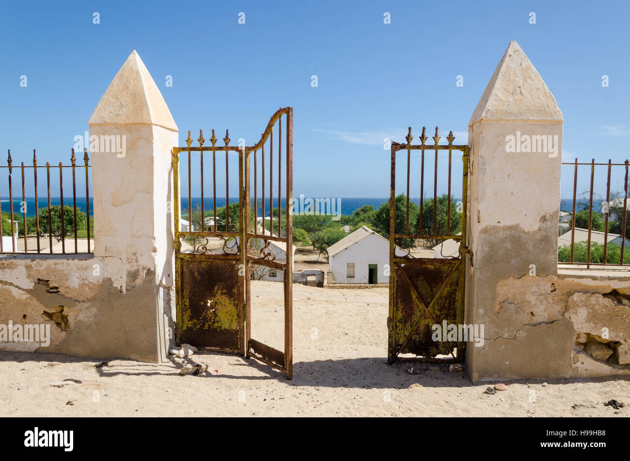 Crumbling metal gate of colonial stone wall overlooking beautiful ocean in small fishing village Mucuio in Angola. Stock Photo