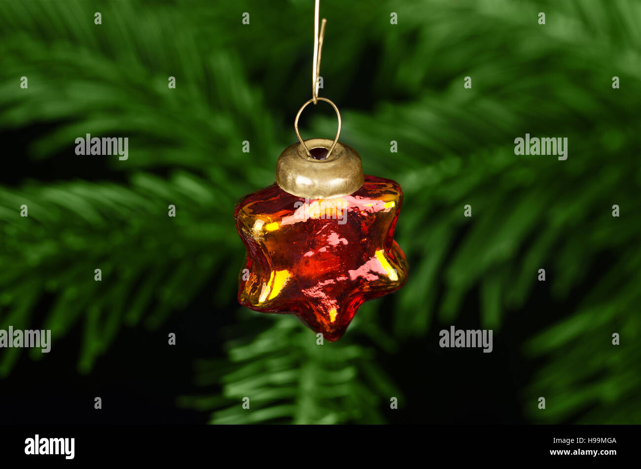 Glass star bauble Christmas tree decoration. Handmade xmas tree ornament, antique, tiny and shiny, in front of a fir branch. Stock Photo