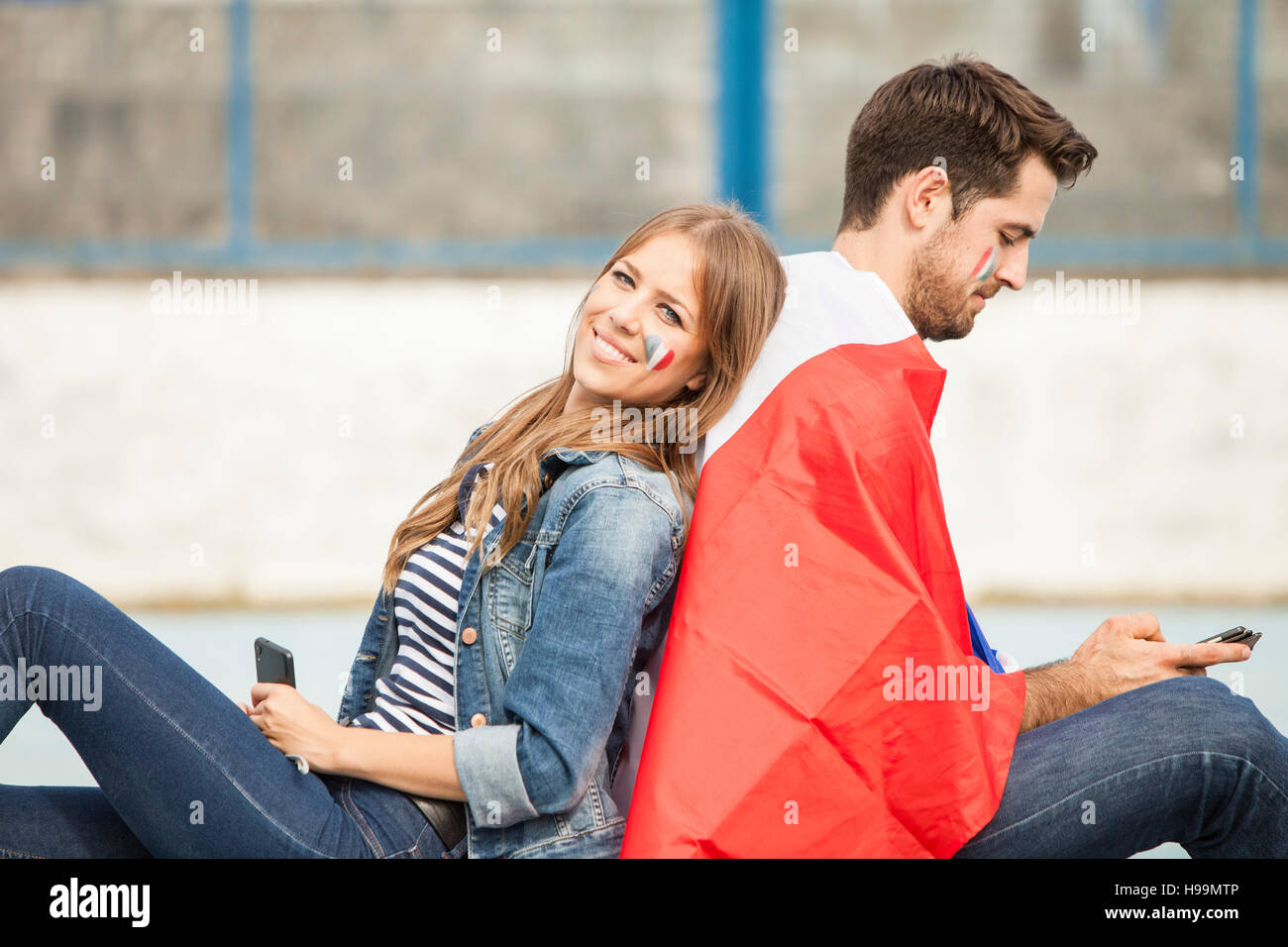 Male soccer fan and girlfriend sitting back to back Stock Photo
