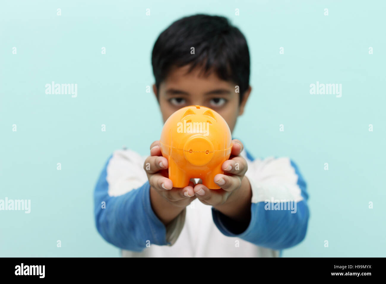 Saving money. Boy holding piggy bank in his hand. He is putting money ...