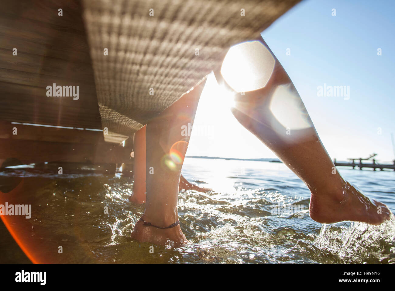 Young women sit on pier bathing feet in water Stock Photo